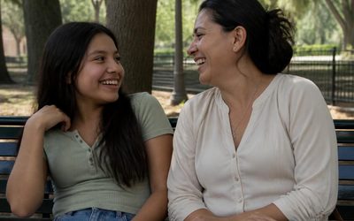 Teenage girl and her mother laughing on a park bench