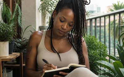 Woman journaling on a plant-filled balcony